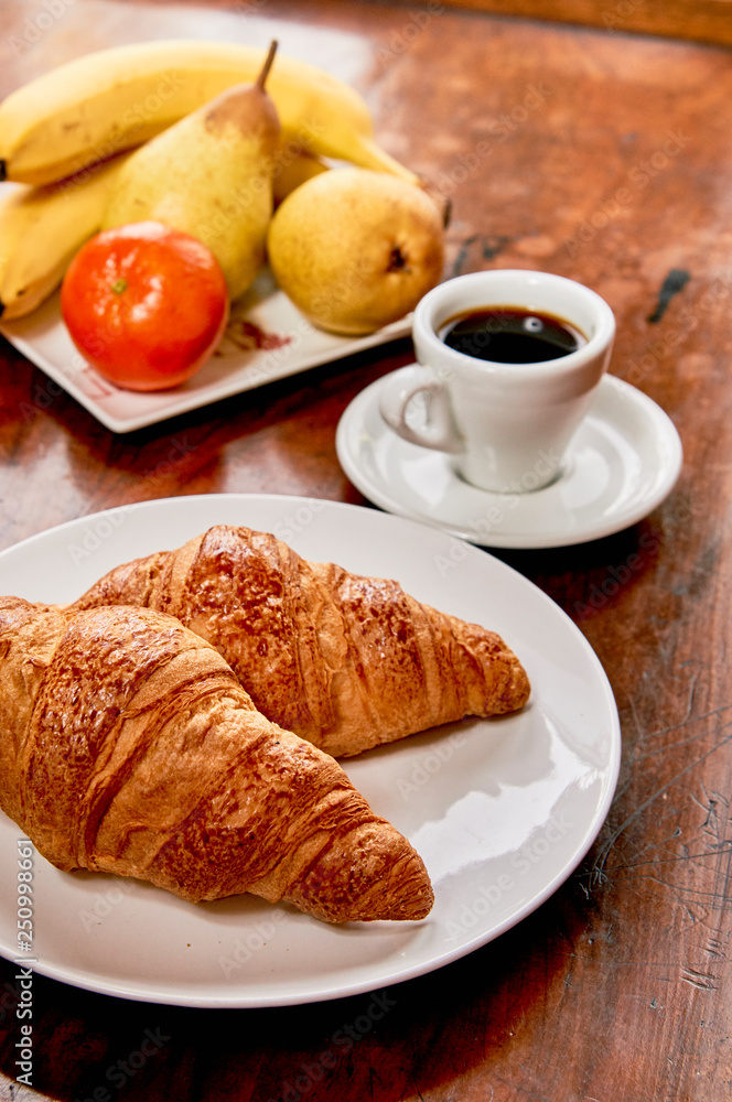 Coffee and croissant breakfast on a vintage wooden table. Espresso, croissants, and fruits. 