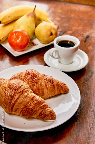 Coffee and croissant breakfast on a vintage wooden table. Espresso, croissants, and fruits. 