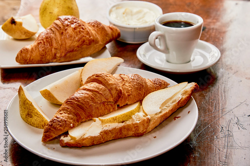 Coffee and croissant breakfast on a vintage wooden table. Espresso, croissants, cream cheese and fruits. 
