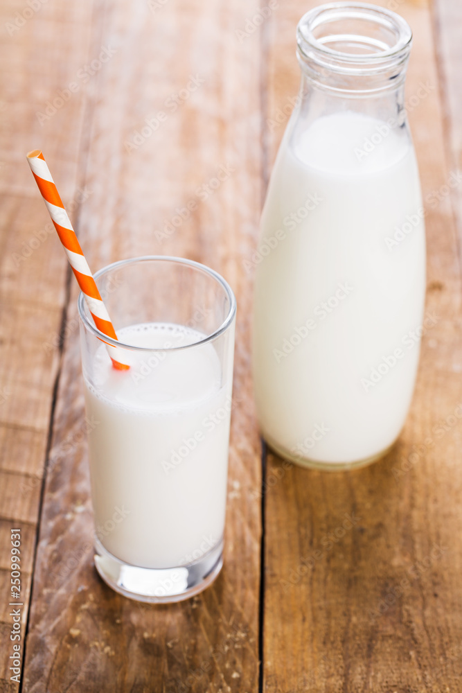 Bottle and glass of milk with straw on wooden table Bottle and glass of milk with straw on wooden table