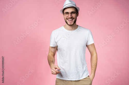 Cheerful hipster guy smiles happily, has excited expression, dresssed casually isolated over pink studio background. People, youth, emotions concept.