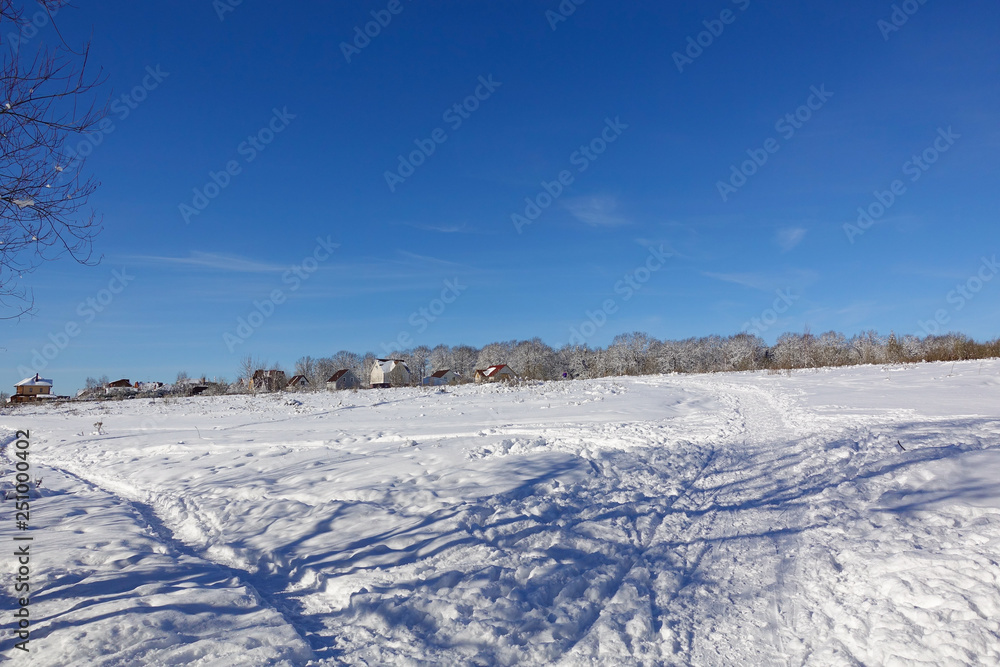 Beautiful winter landscape. Village near the forest. Blue sky and snowy field. Frosty sunny day. Russia