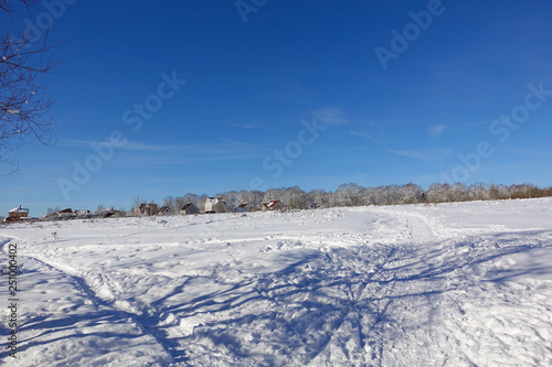 Beautiful winter landscape. Village near the forest. Blue sky and snowy field. Frosty sunny day. Russia