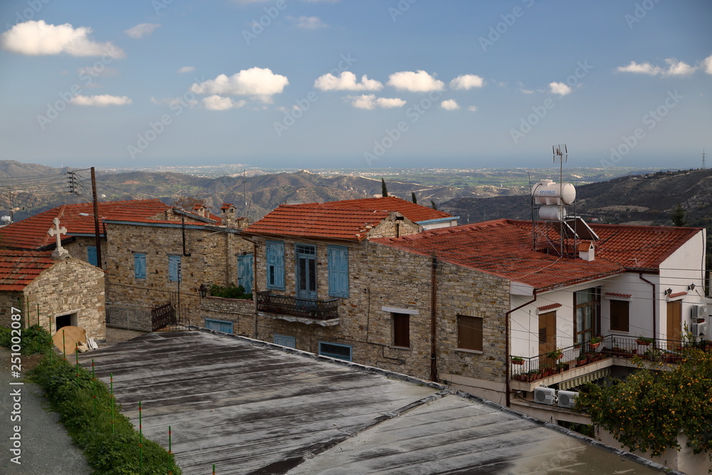 Traditional stony houses with blue shutters and red roofs in lefkara, mountains village in cyprus, hills in background, blue sky with few white clouds