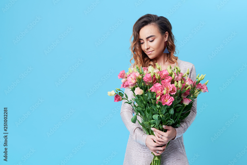 Young happy smiling redhead woman holding bouquet of colorful spring flowers isolated on blue background Young happy smiling redhead woman holding bouquet of colorful spring flowers isolated on blue background