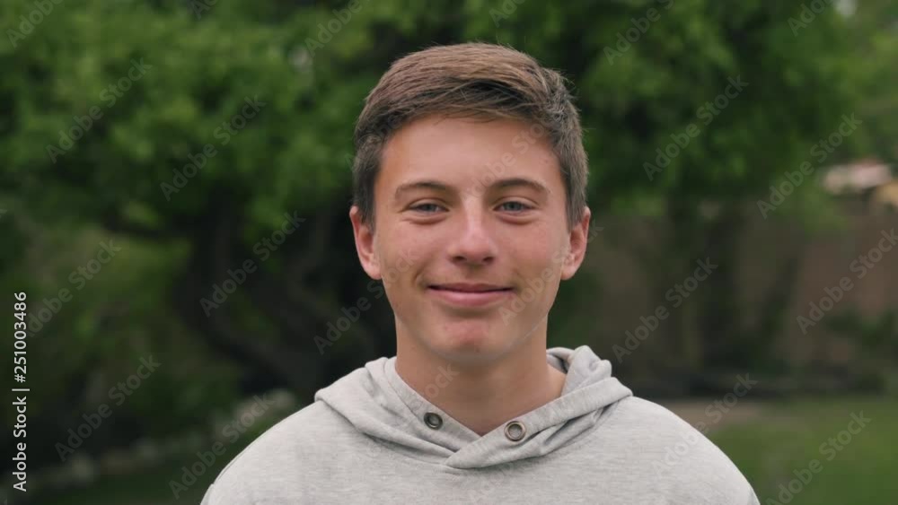 Portrait of a young white male teenager holding back his laughter in the outdoors Portrait of a young white male teenager holding back his laughter in the outdoors