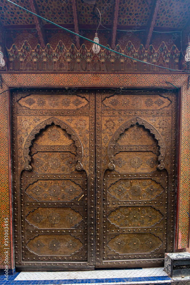 Traditional Moroccan style design of an ancient wooden entry door. In the old Medina of Marrakech, Morocco. Typical, old, brown intricately carved, studded, Moroccan riad door
