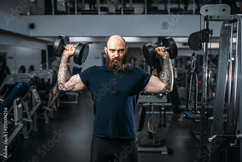 Muscular athlete poses with dumbbells in gym