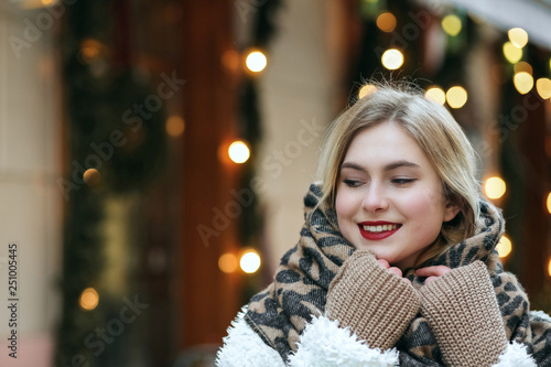 Wallpaper Mural Joyful blonde model wears winter coat and knit scarf walking at the city. Space for text Torontodigital.ca