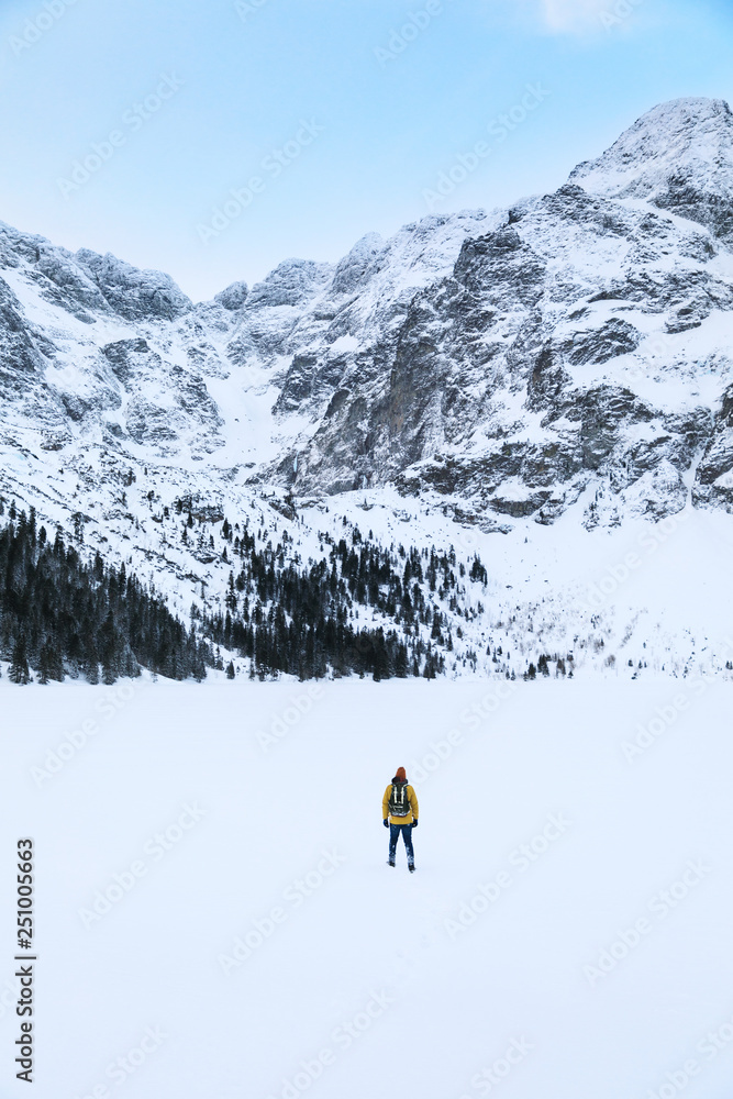 The traveler is walking on ice of the Lake of Morskie Oko in winter mountains