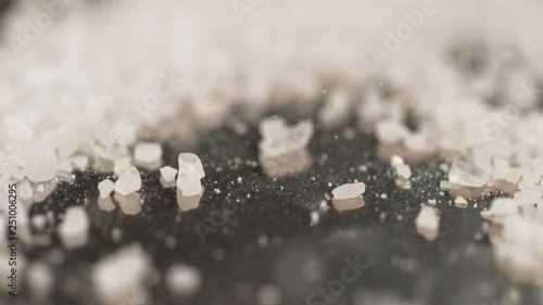 SLOW MOTION, MACRO, DOF: Pristine white salt crystals are sprinkled across the black surface of the chef's table. Cool shot of sugar crystals fall and bounce around the granite kitchen countertop. photo