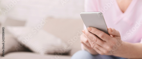 Cheerful aged woman using her smartphone at home