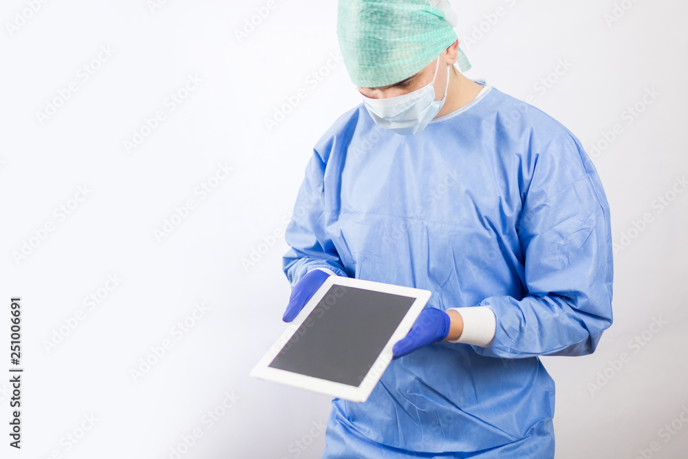 Surgeon doctor in sterile gloves preparing for operation using tablet computer. He is wearing surgical cap and blue gown Surgeon doctor in sterile gloves preparing for operation using tablet computer. He is wearing surgical cap and blue gown