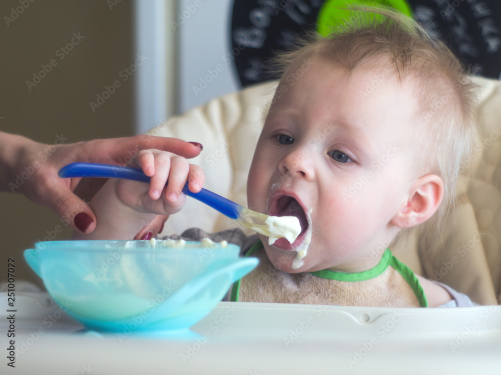 baby learns to eat yourself with a spoon. one year old boy eats porridge from a plate baby learns to eat yourself with a spoon. one year old boy eats porridge from a plate
