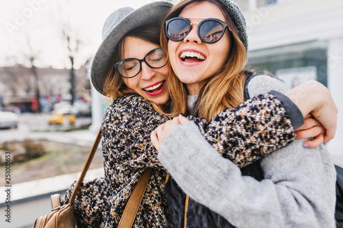Happy brightful positive moments of two stylish girls hugging on street in city. Closeup portrait funny joyful attarctive young women having fun, smiling, lovely moments, best friends photo