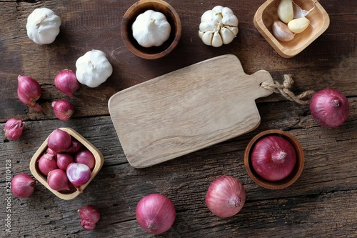 Assorted fresh organic red onion and garlic on cutting board on wooded background, herb cooking preparation concept, top view