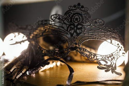 Black lace mask is on the table in a romantic atmosphere. Backlight, close-up.