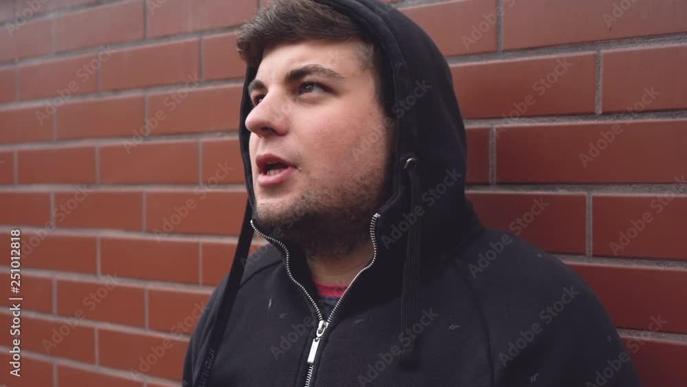 Young caucasian man in a hooded sweatshirt smoking cigarette leaning against red brick wall. Young caucasian man in a hooded sweatshirt smoking cigarette leaning against red brick wall.