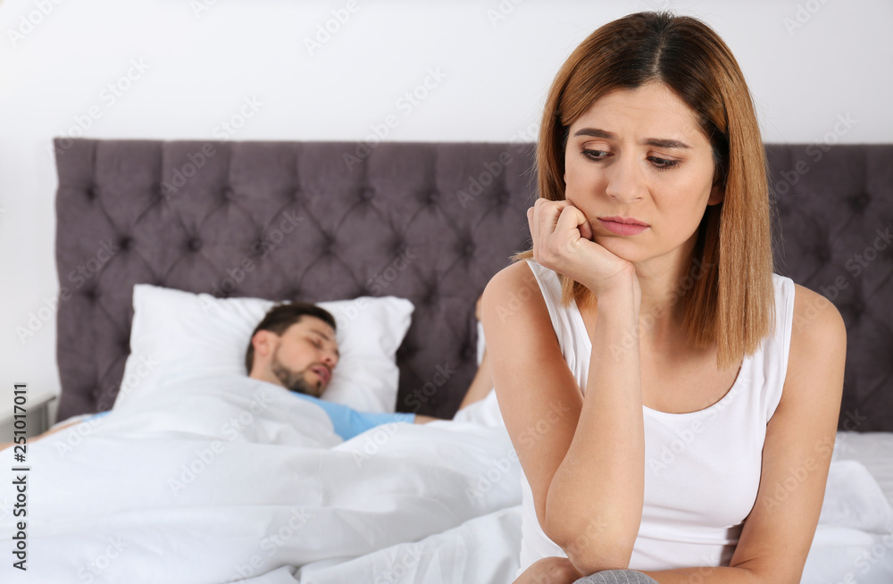 Upset woman sitting on bed near her sleeping husband at home. Relationship problems Upset woman sitting on bed near her sleeping husband at home. Relationship problems