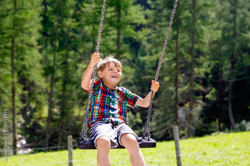 Funny kid boy having fun with chain swing on outdoor playground while being wet splashed with water. child swinging on summer day. Active leisure with kids. Happy crying boy with rain drops on face.