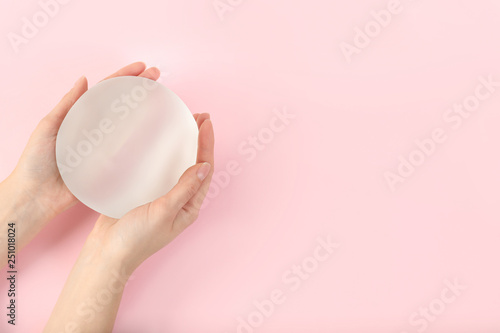 Woman holding silicone implant for breast augmentation on color background, top view with space for text. Cosmetic surgery photo