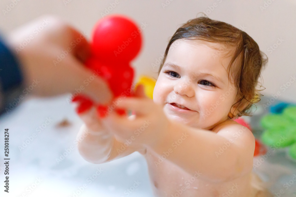 Cute adorable baby girl taking foamy bath in bathtub. Toddler playing with bath rubber toys. Beautiful child having fun with colorful gum toys and foam bubbles Cute adorable baby girl taking foamy bath in bathtub. Toddler playing with bath rubber toys. Beautiful child having fun with colorful gum toys and foam bubbles