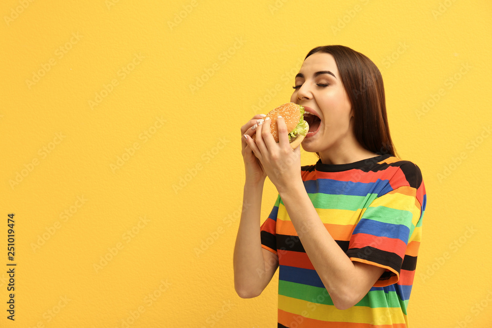 Young woman eating tasty burger on color background. Space for text