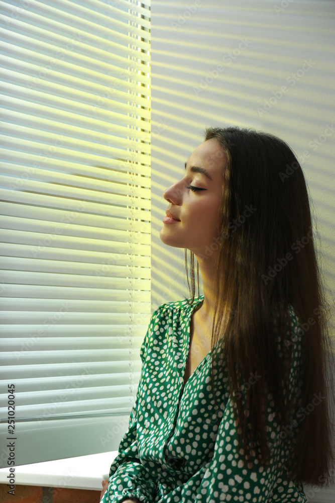 Young woman near window with Venetian blinds Young woman near window with Venetian blinds