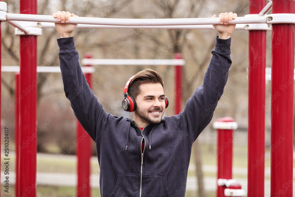Naklejka premium Young man with headphones listening to music and exercising on sports ground
