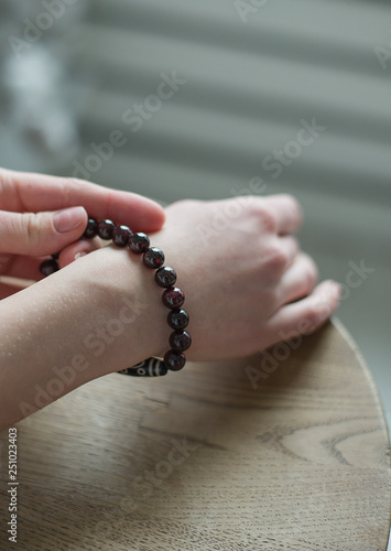 bracelet of dark red, black stones, a bracelet of stones (garnet), the girl touches the stones on the bracelet (close up, vertically).