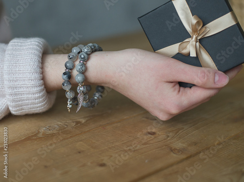 girl holds a gift box tied with a ribbon, on her arm are two tourmaline bracelets, a bracelet made of gray stones (horizontally, close up).
