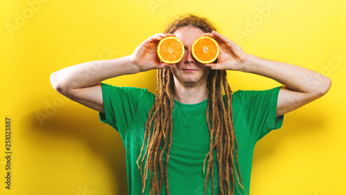 Happy young man holding oranges on a yellow background © Tierney