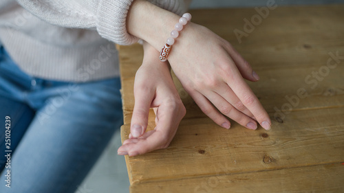 the girl on her arm has a bracelet made of pink stones (quartz), a bracelet made of quartz, hands, wooden table  (horizontally, light toned)