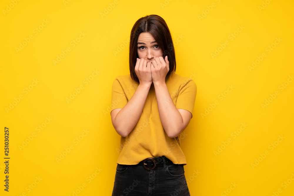 Young woman over yellow wall nervous and scared putting hands to mouth Young woman over yellow wall nervous and scared putting hands to mouth