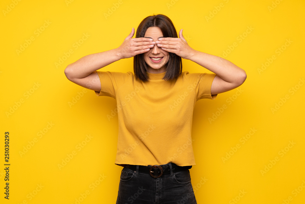 Young woman over yellow wall covering eyes by hands. Surprised to see what is ahead Young woman over yellow wall covering eyes by hands. Surprised to see what is ahead