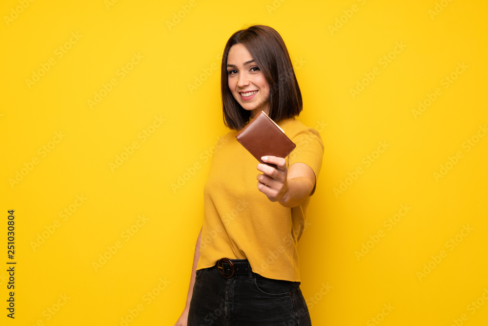 Young woman over yellow wall holding a wallet Young woman over yellow wall holding a wallet