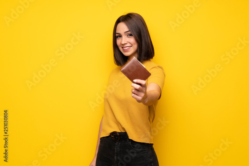 Young woman over yellow wall holding a wallet photo