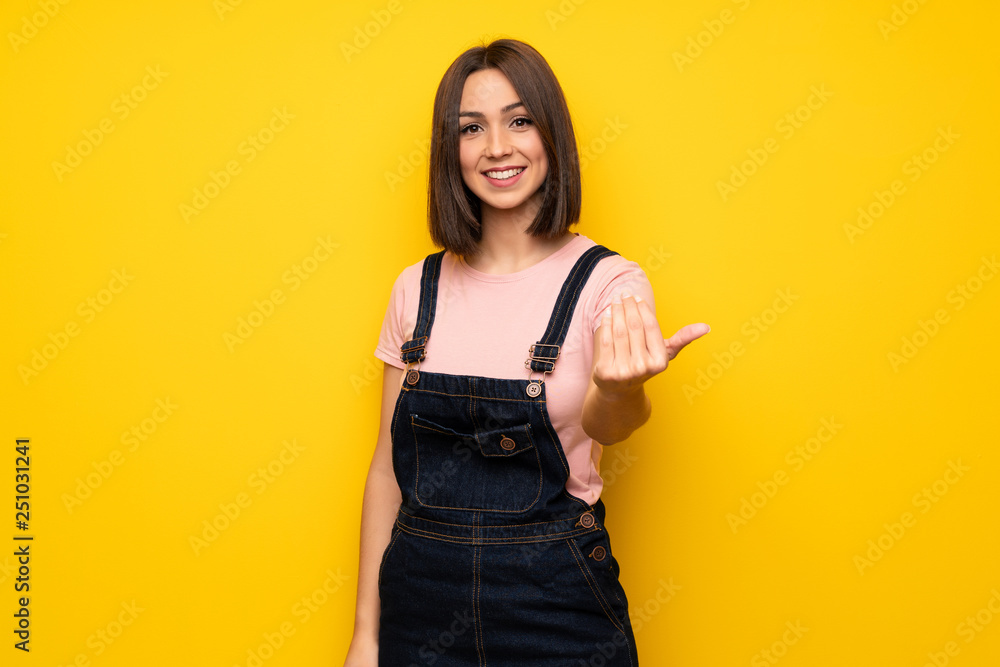 Young woman over yellow wall inviting to come with hand. Happy that you came Young woman over yellow wall inviting to come with hand. Happy that you came