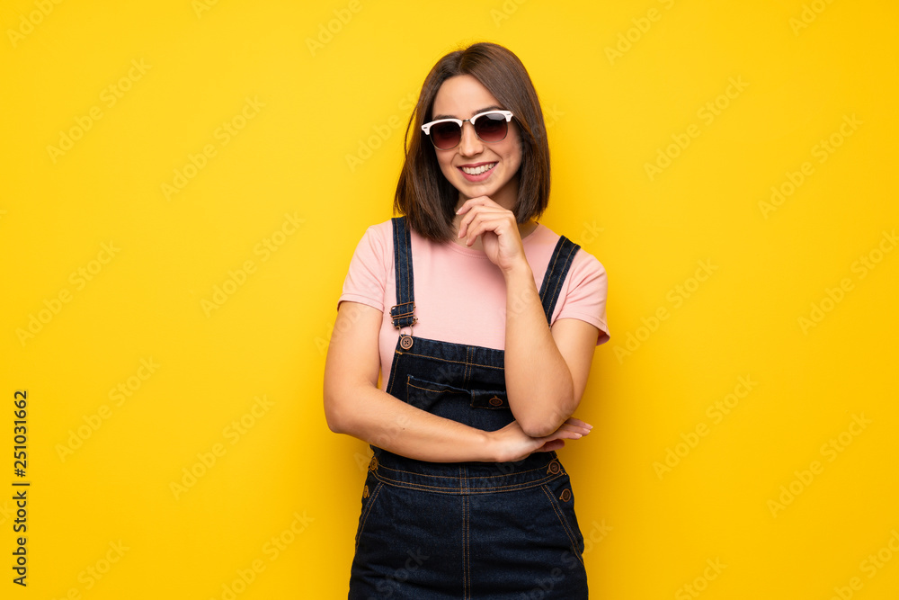 Young woman over yellow wall with glasses and smiling
