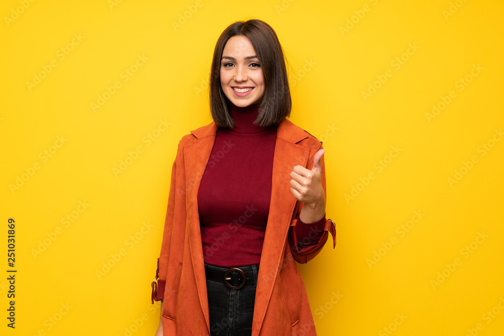 Young woman with coat giving a thumbs up gesture and smiling Young woman with coat giving a thumbs up gesture and smiling