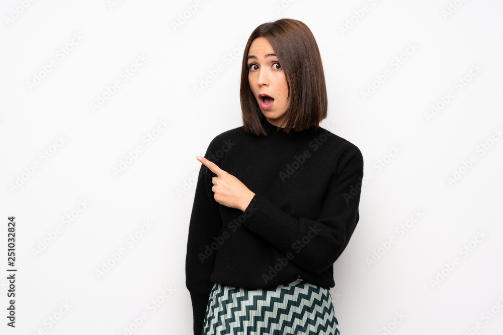 Young woman over white wall surprised and pointing side Young woman over white wall surprised and pointing side