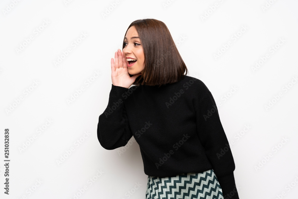Young woman over white wall shouting with mouth wide open to the lateral Young woman over white wall shouting with mouth wide open to the lateral