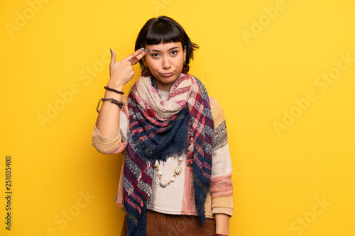 Young hippie woman over yellow wall with problems making suicide gesture