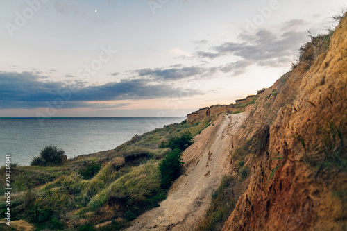 Beautiful view of sandy cliff near sea beach in sunset. Landscape of beach cliff and waves and cloudy sky in sunset or sunrise. Summer vacation concept. Exploring interesting places