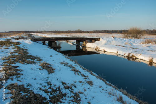 Bridge on the river and snow in the meadows
