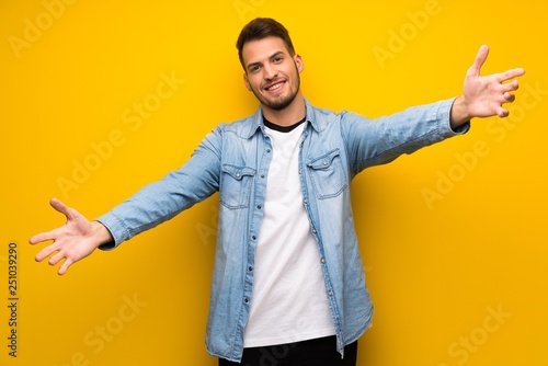 Handsome man over yellow wall presenting and inviting to come with hand