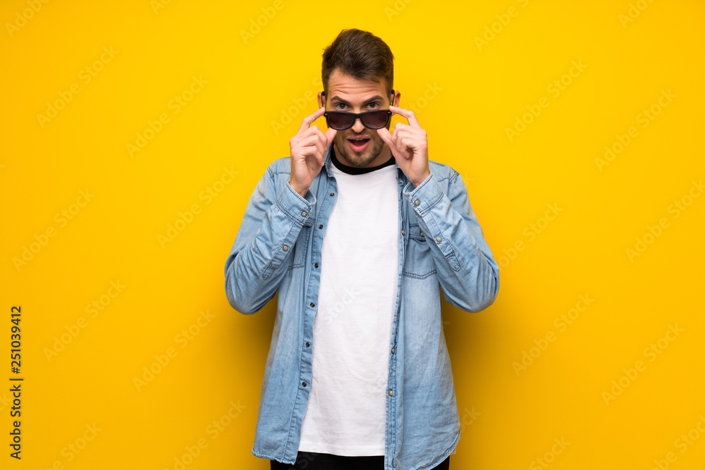 Handsome man over yellow wall with glasses and surprised Handsome man over yellow wall with glasses and surprised