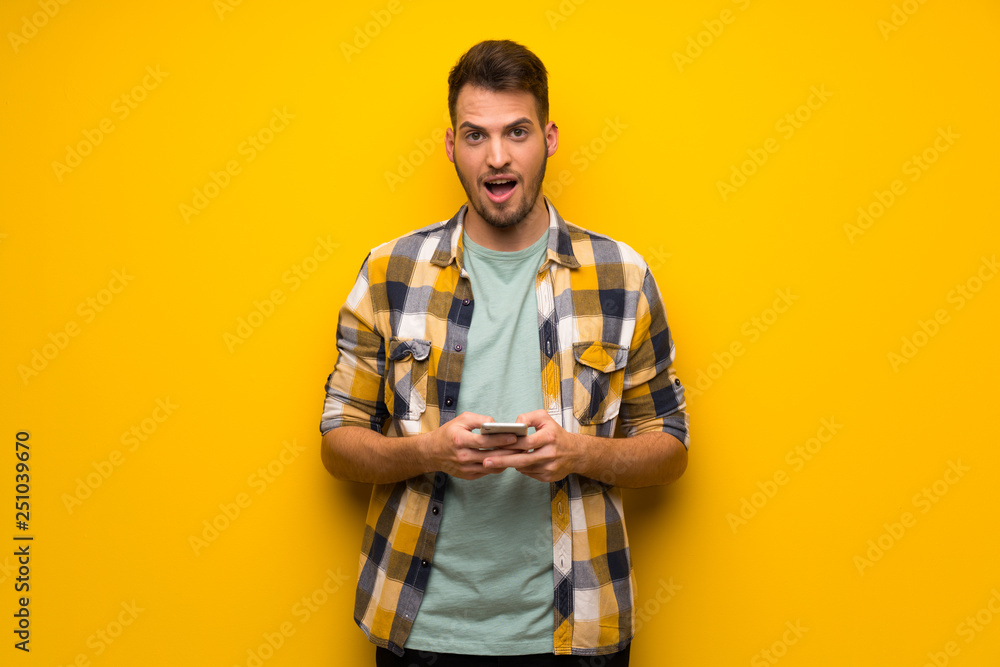 Handsome man over yellow wall surprised and sending a message Handsome man over yellow wall surprised and sending a message