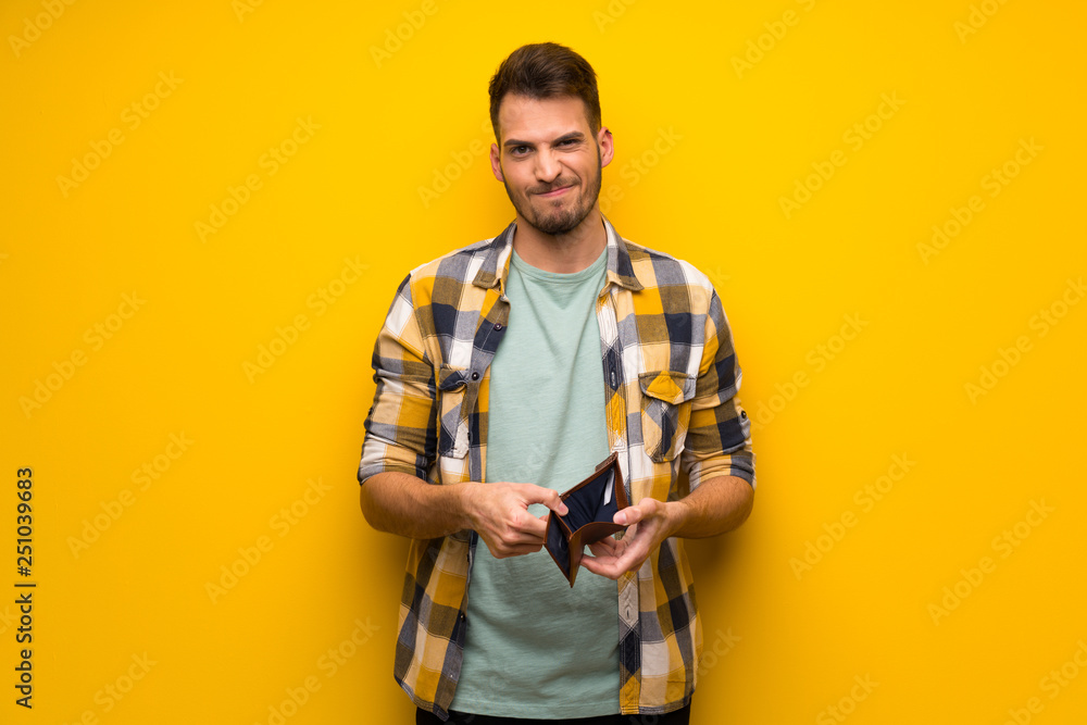 Handsome man over yellow wall holding a wallet Handsome man over yellow wall holding a wallet