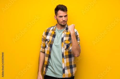 Handsome man over yellow wall with angry gesture